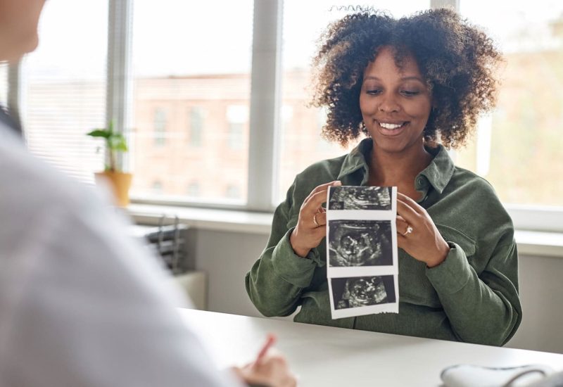 pregnant woman holding sonogram pictures smiling